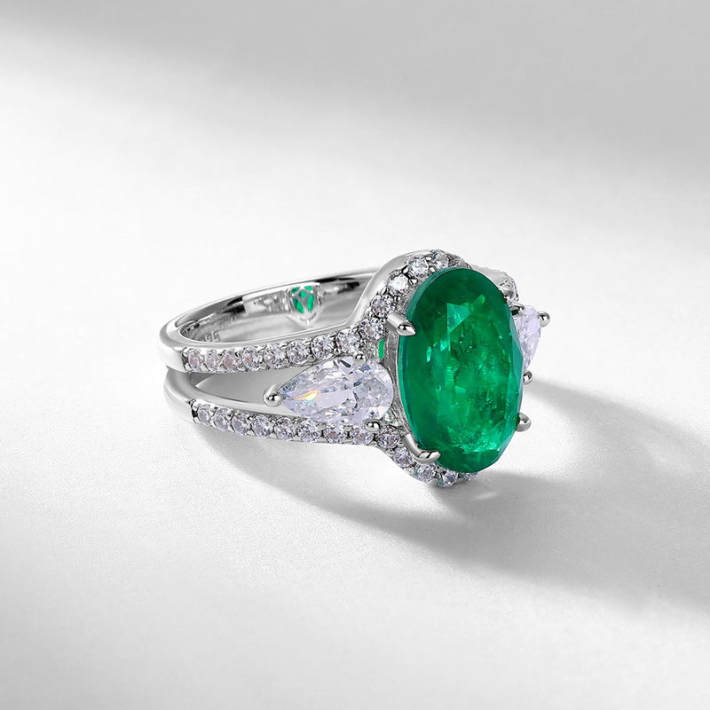 Three-quarter studio product view of a classic oval-cut emerald halo ring casting a crisp gradient shadow.