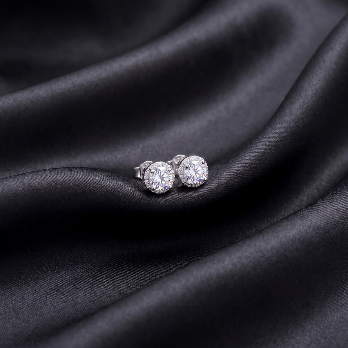 Classic round cut lab grown diamond halo stud earrings resting on dark black silk