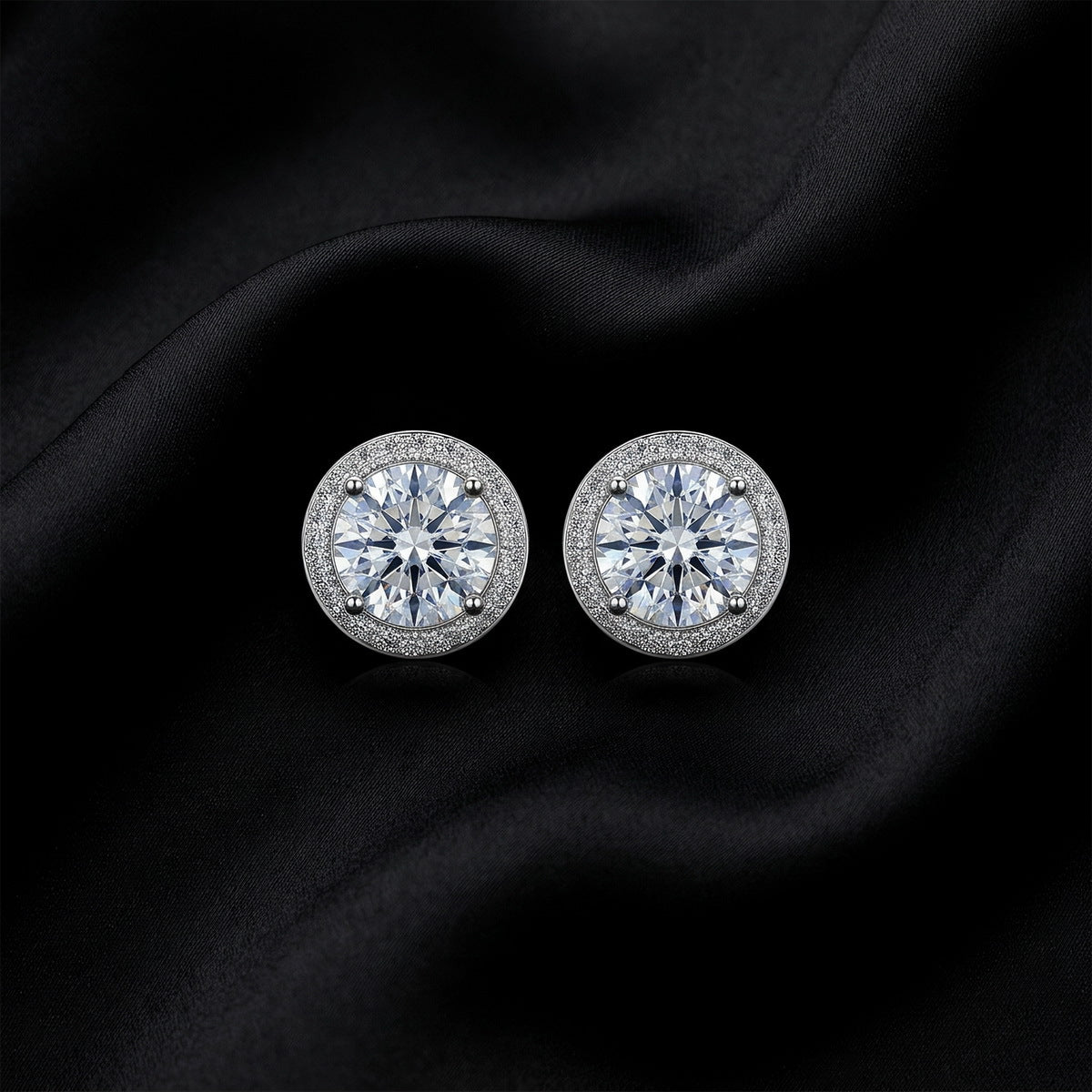 Frontal top view of pair of round halo lab grown diamond stud earrings on dark black silk