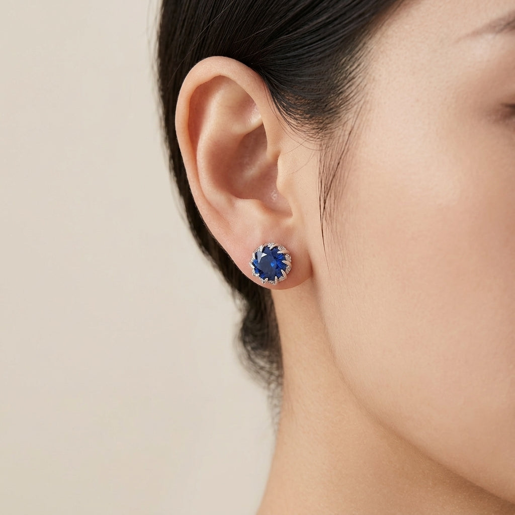 Close-up of an ear wearing a blue gemstone earring on a neutral background