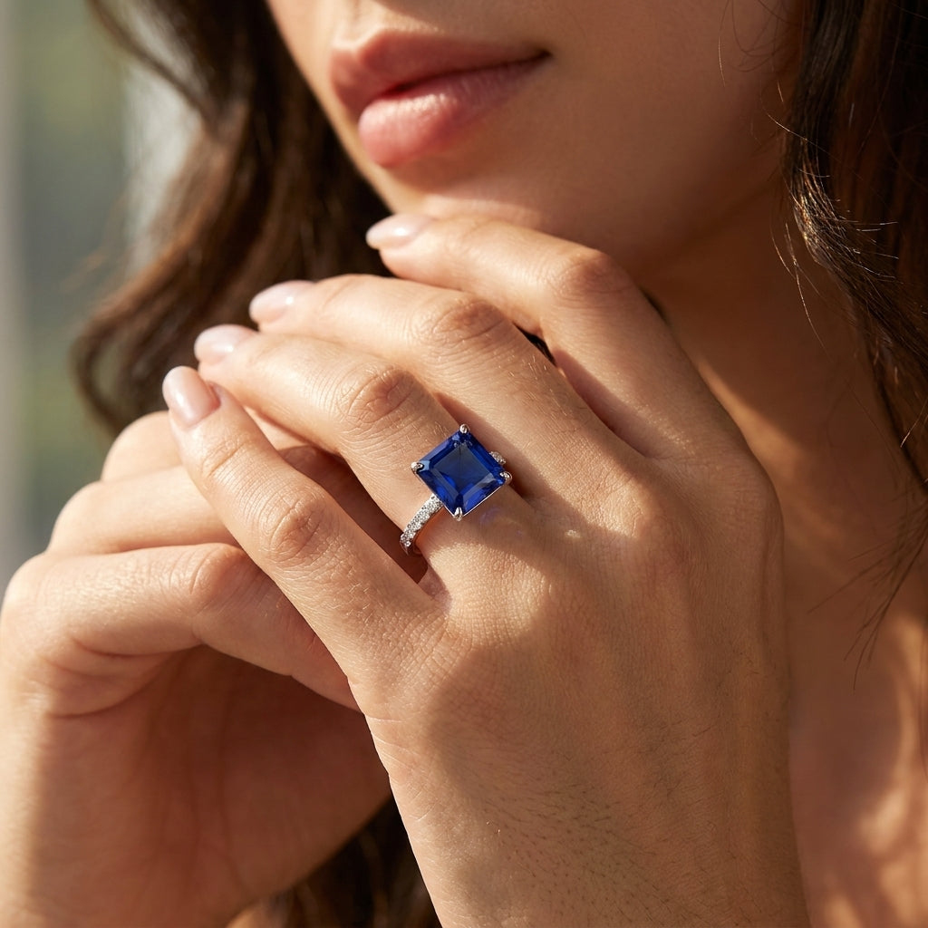 Close-up of an elegant model showcasing the large square-cut blue sapphire statement ring under soft studio lighting.