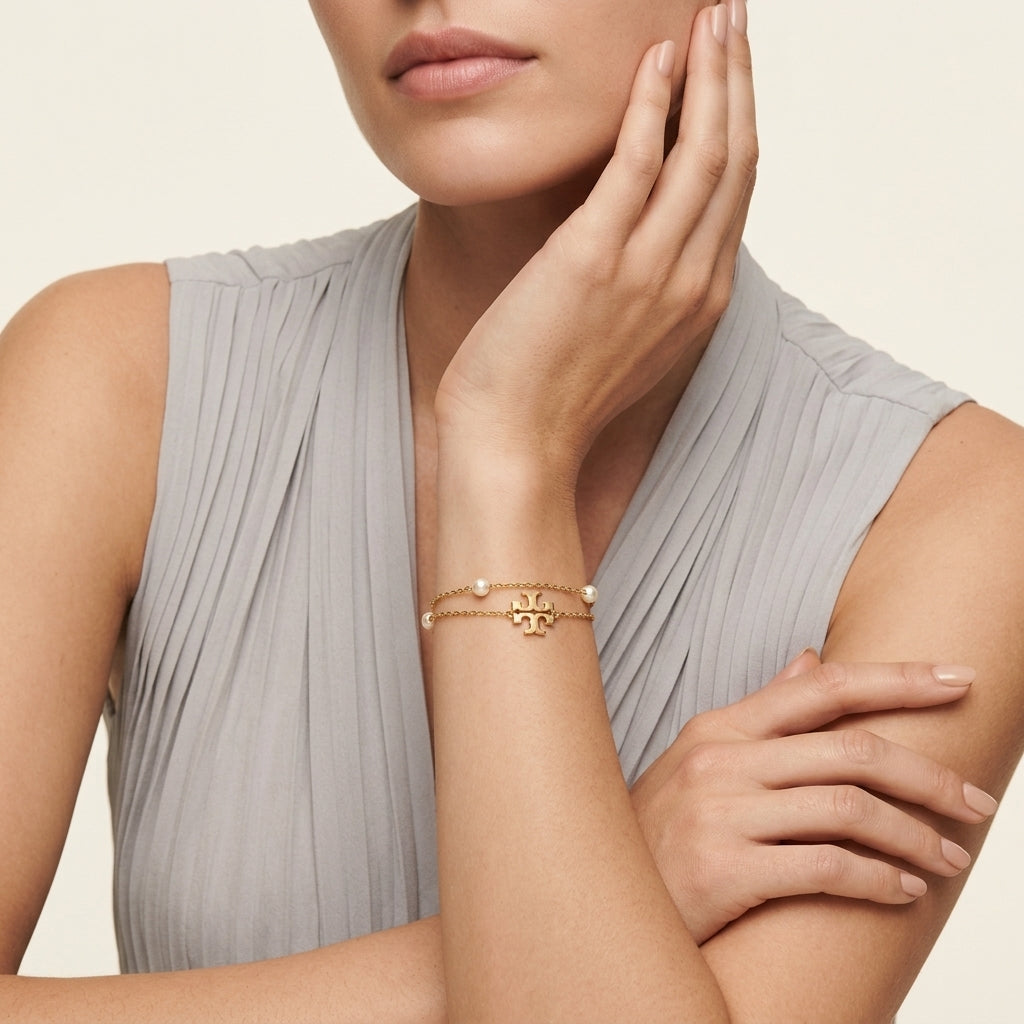 High-end fashion lookbook view of a model's wrist gracefully wearing classic Tory Burch double T layered pearl bracelet.
