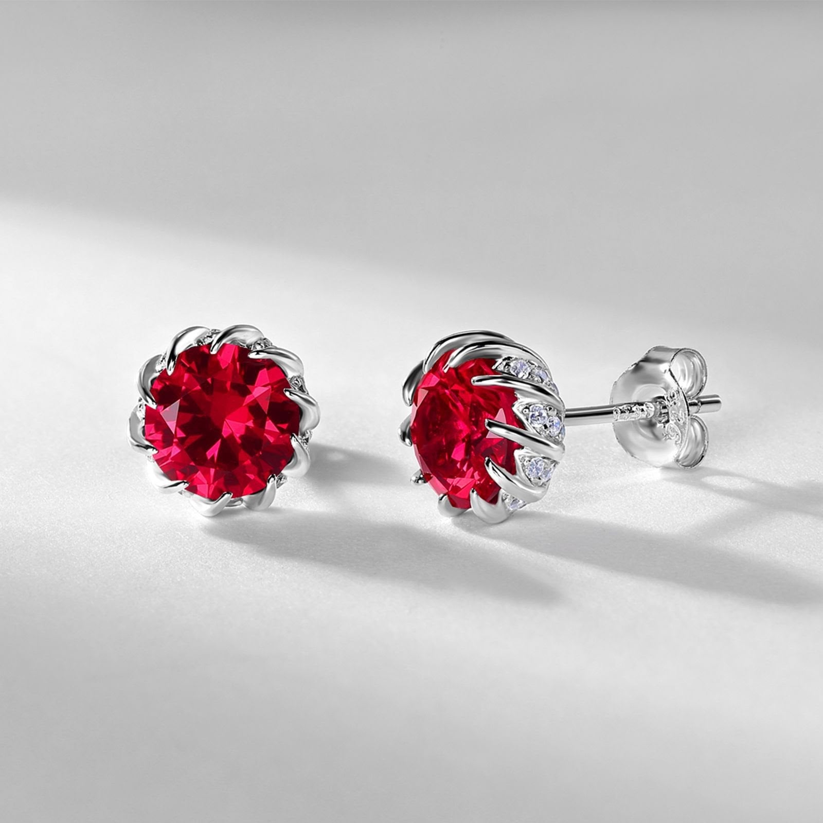Pair of silver earrings with red gemstones on a light gray background