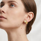 Lifestyle fashion lookbook portrait of a model styling 18k gold puffy heart moissanite stud earrings near her neck.