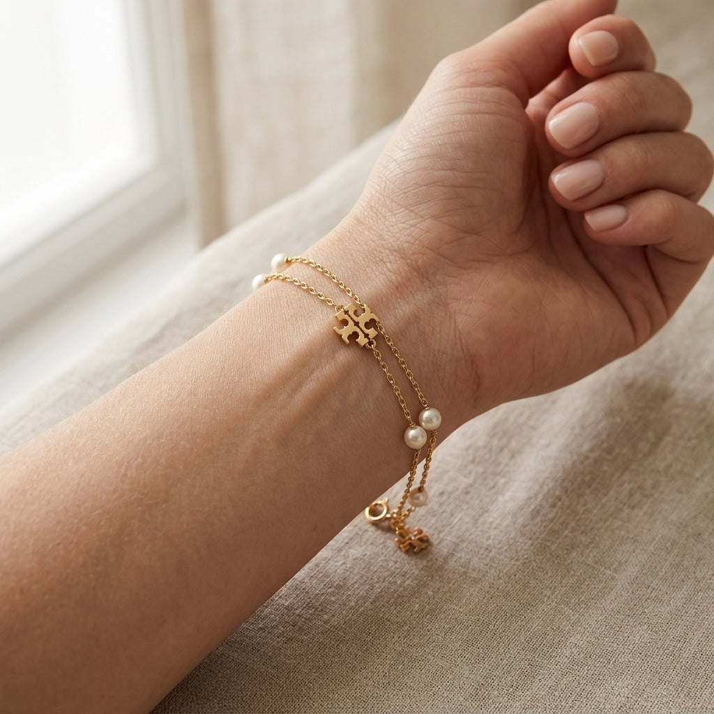 Lifestyle fashion lookbook portrait of a model styling designer gold tone layered pearl bracelet on wrist over a sofa background.