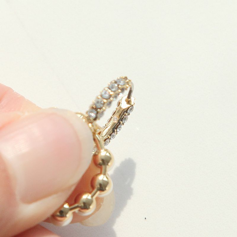 Detailed macro shot of a hand holding a designer style crystal paved white pearl hoop earring to demonstrate the premium clasp.
