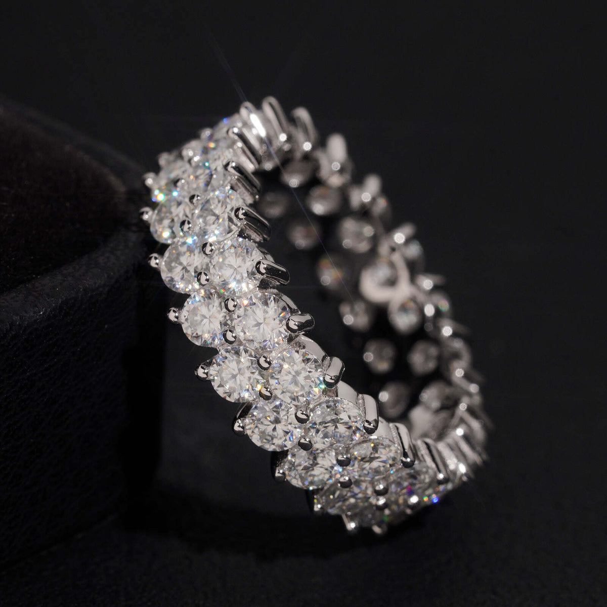 Angled view of double row round moissanite full eternity band ring on dark background