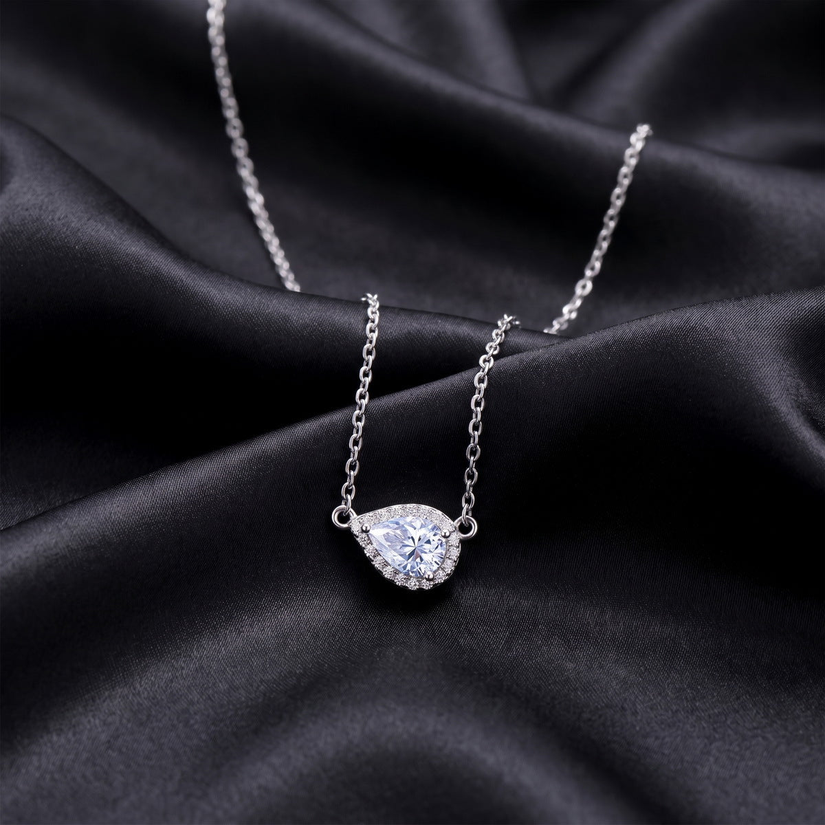 East-west pear cut moissanite halo pendant necklace resting on black silk fabric   
