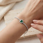 Side angle view of a model wearing an elegant cushion emerald halo bracelet resting on a beige stone surface.