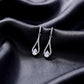 Pair of pear cut lab grown diamond teardrop earrings displayed on dark black silk fabric