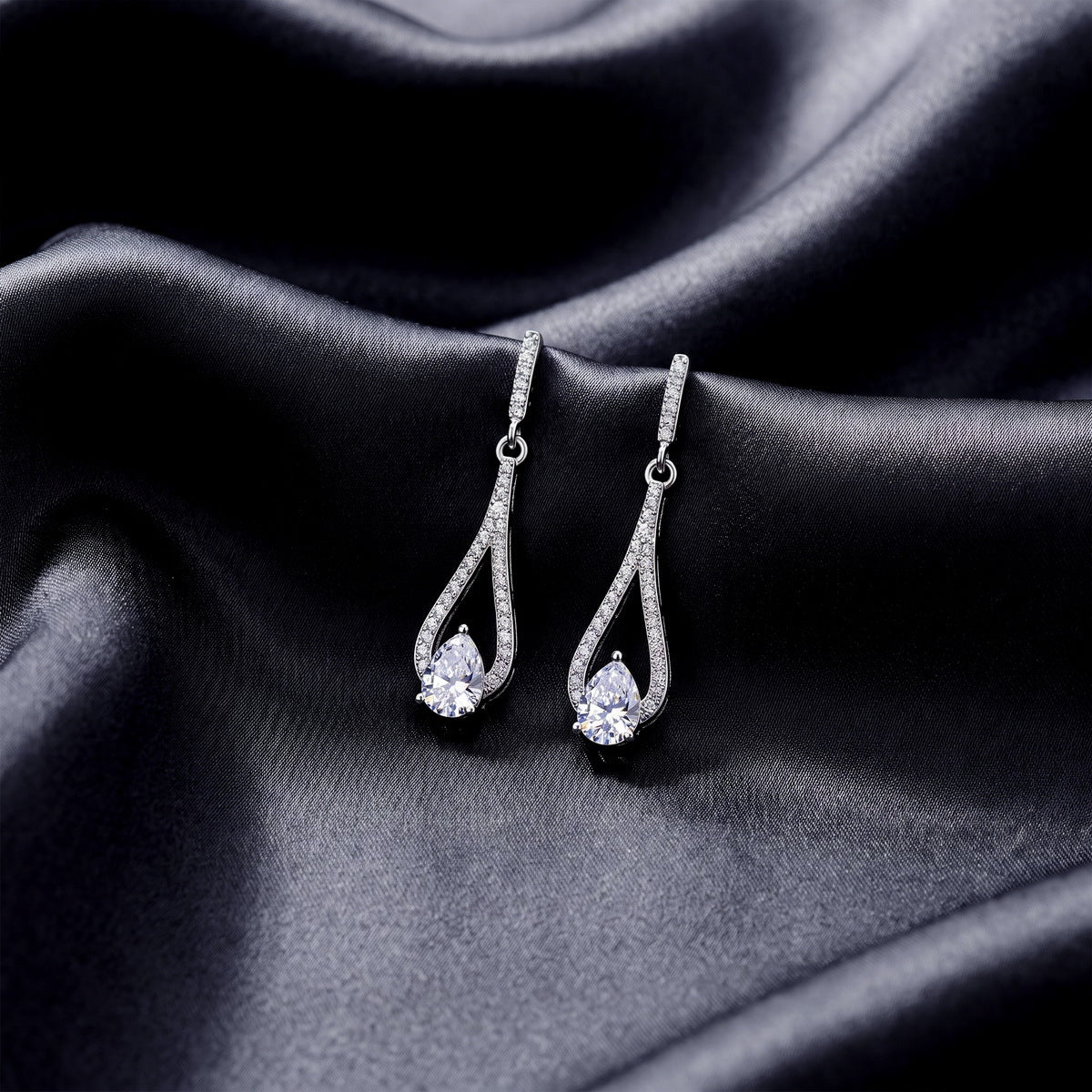 Pair of pear cut lab grown diamond teardrop earrings displayed on dark black silk fabric