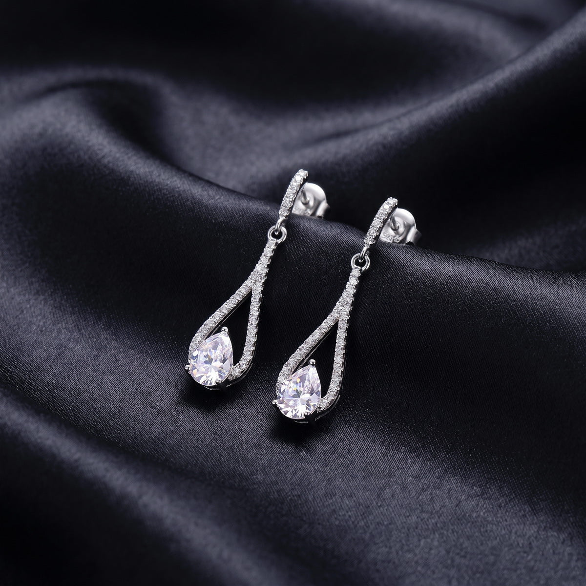 Angled side view of pear cut lab grown diamond teardrop drop earrings on black silk