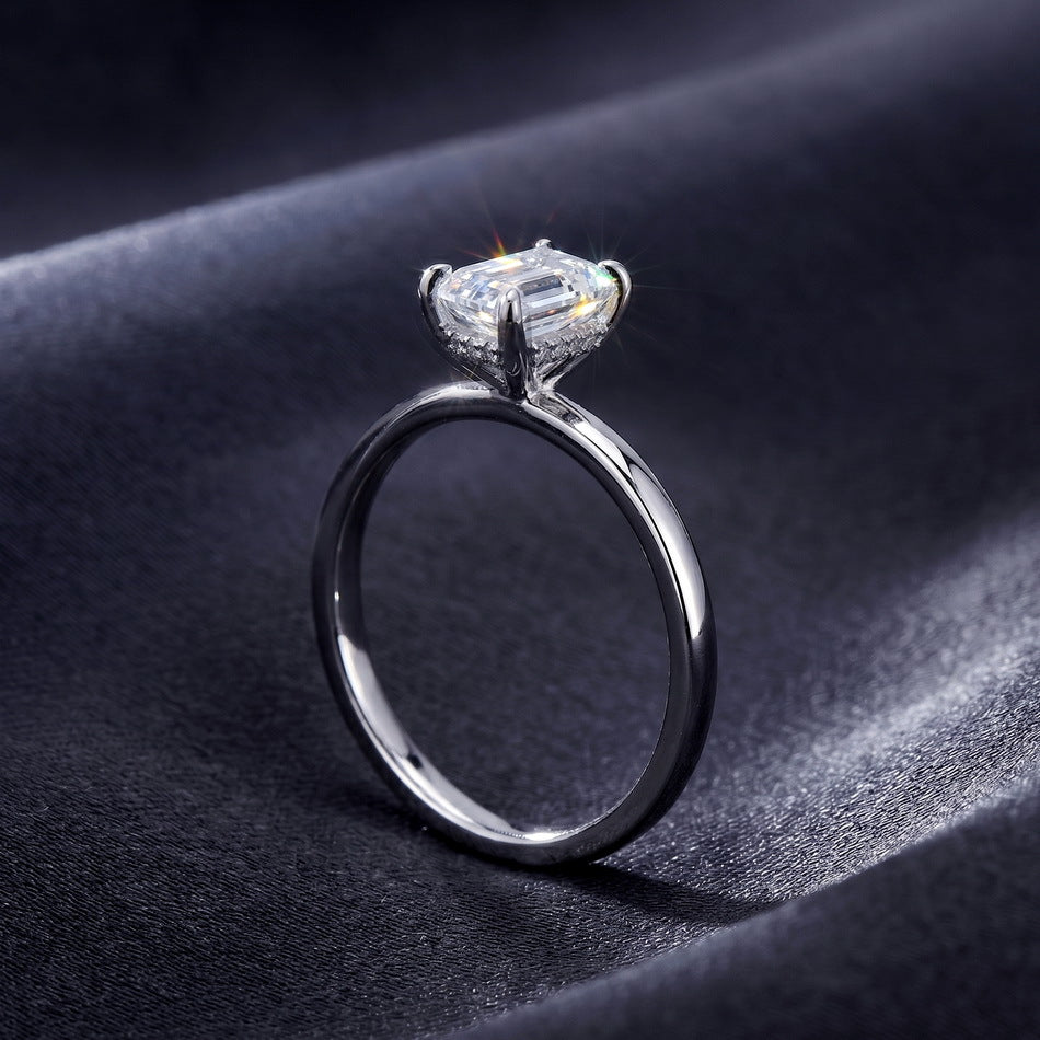 Side perspective shot of emerald cut hidden halo solitaire ring resting on dark silk.