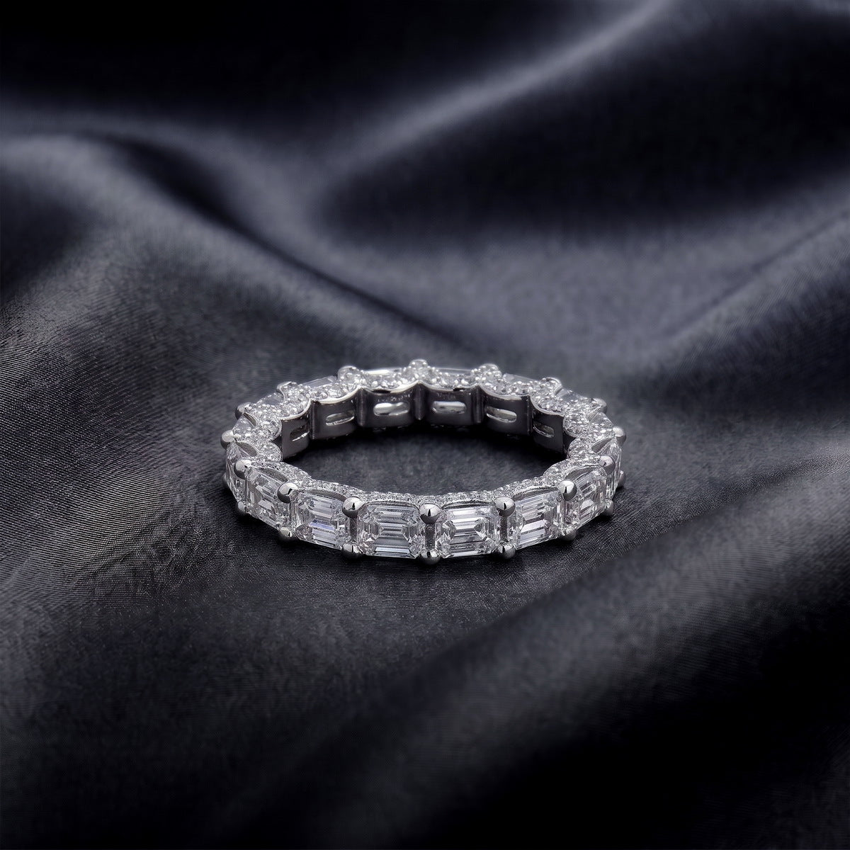 Perspective view of emerald cut lab diamond full eternity wedding band ring on dark silk.