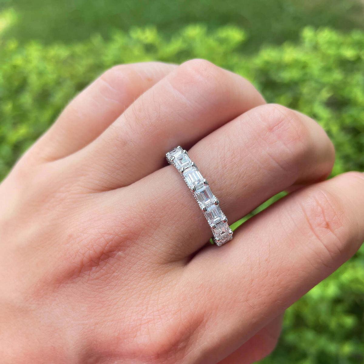 Close-up hand view of emerald cut lab diamond full eternity wedding band ring in natural sunlight.