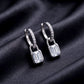 Pair of emerald cut lab grown diamond padlock dangle huggie earrings resting on dark black silk