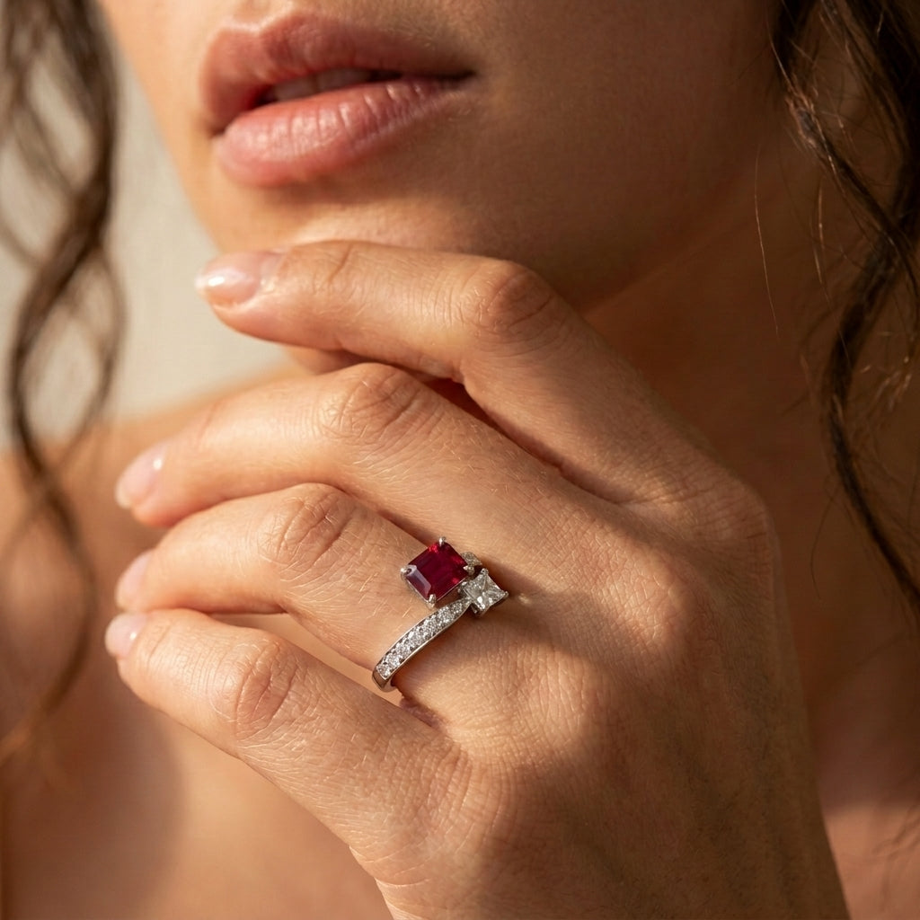 Close-up lifestyle view of a model wearing an emerald-cut ruby and princess-cut diamond Toi et Moi ring on her finger.
