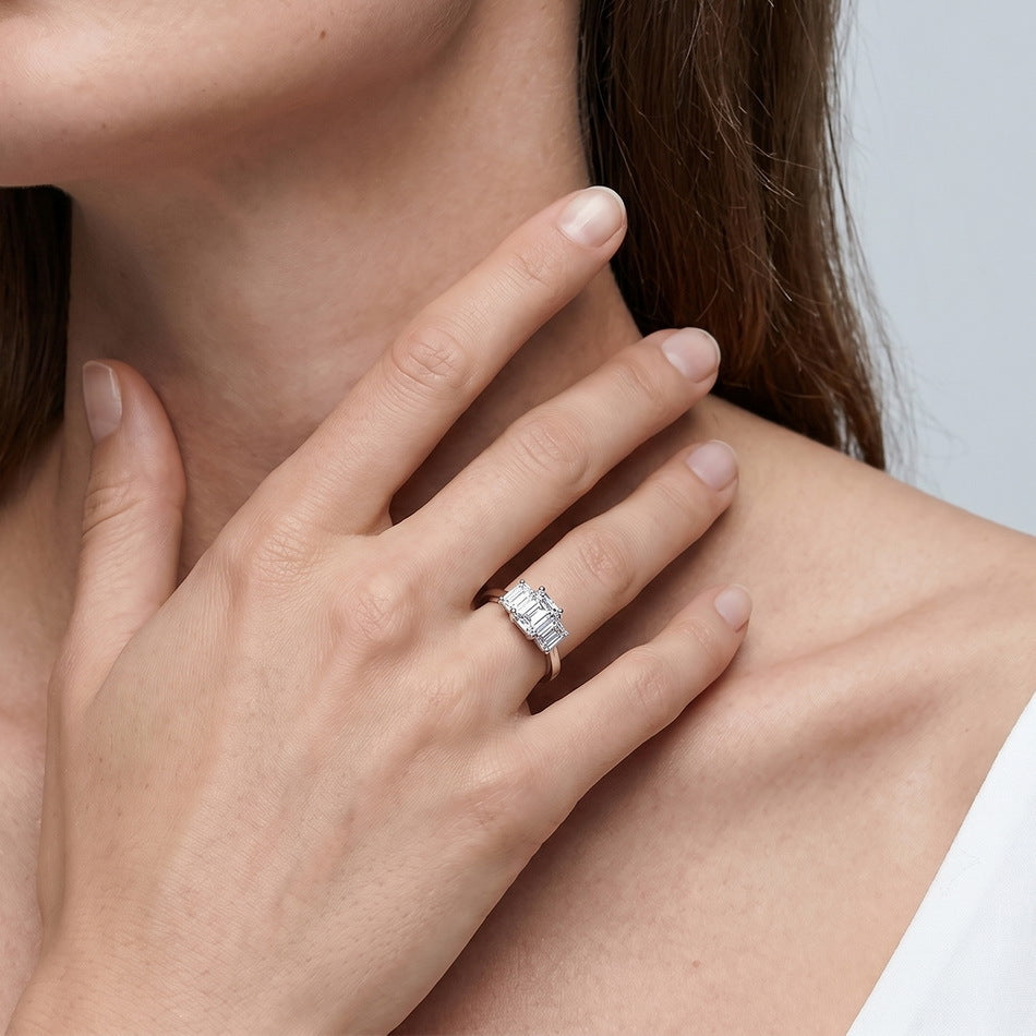 Model wearing emerald cut lab grown diamond three stone engagement ring.