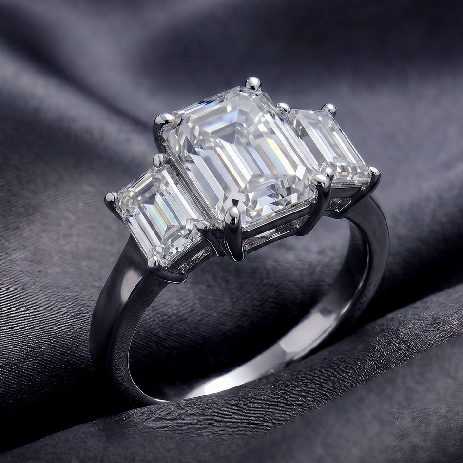 Perspective shot of emerald cut lab grown diamond three stone ring on dark silk.