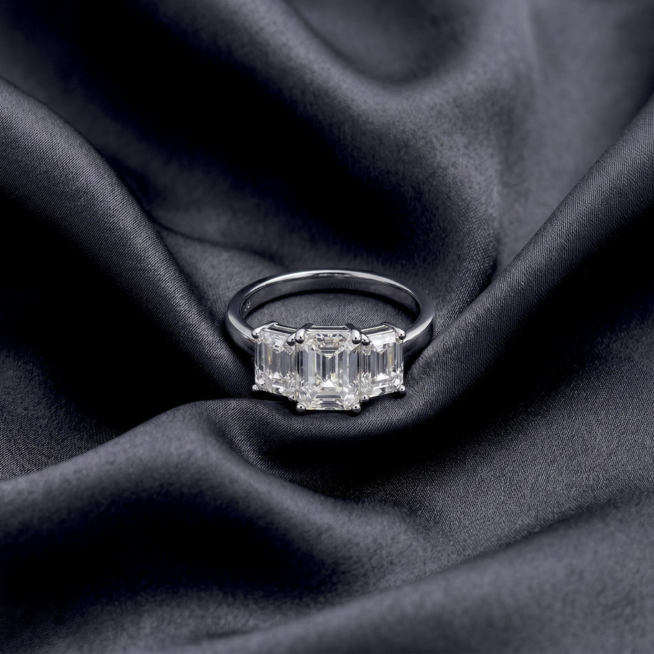 Full profile view of emerald cut lab grown diamond three stone ring on silk.