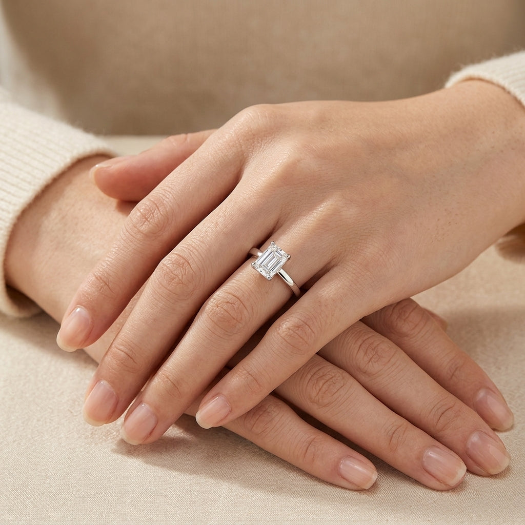 Model showing emerald cut moissanite solitaire ring on hand in warm ambient lighting.