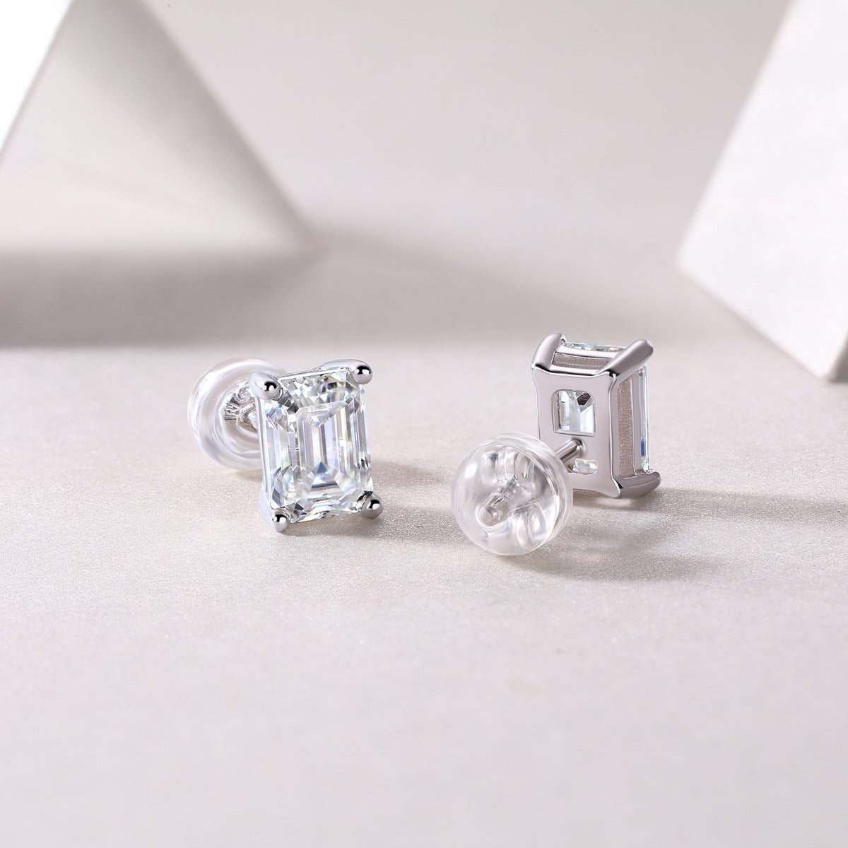 Side profile view showing basket setting and silicone backs on emerald cut moissanite studs.