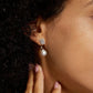 Model wearing emerald and pear cut halo lab grown diamond drop earrings on earlobe