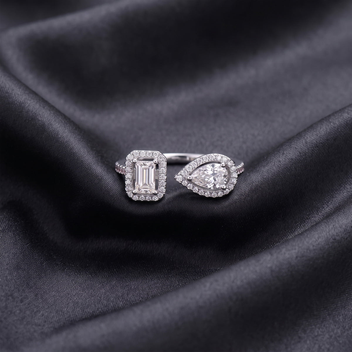 Front view of emerald and pear cut lab grown diamond toi et moi halo ring on dark black silk fabric