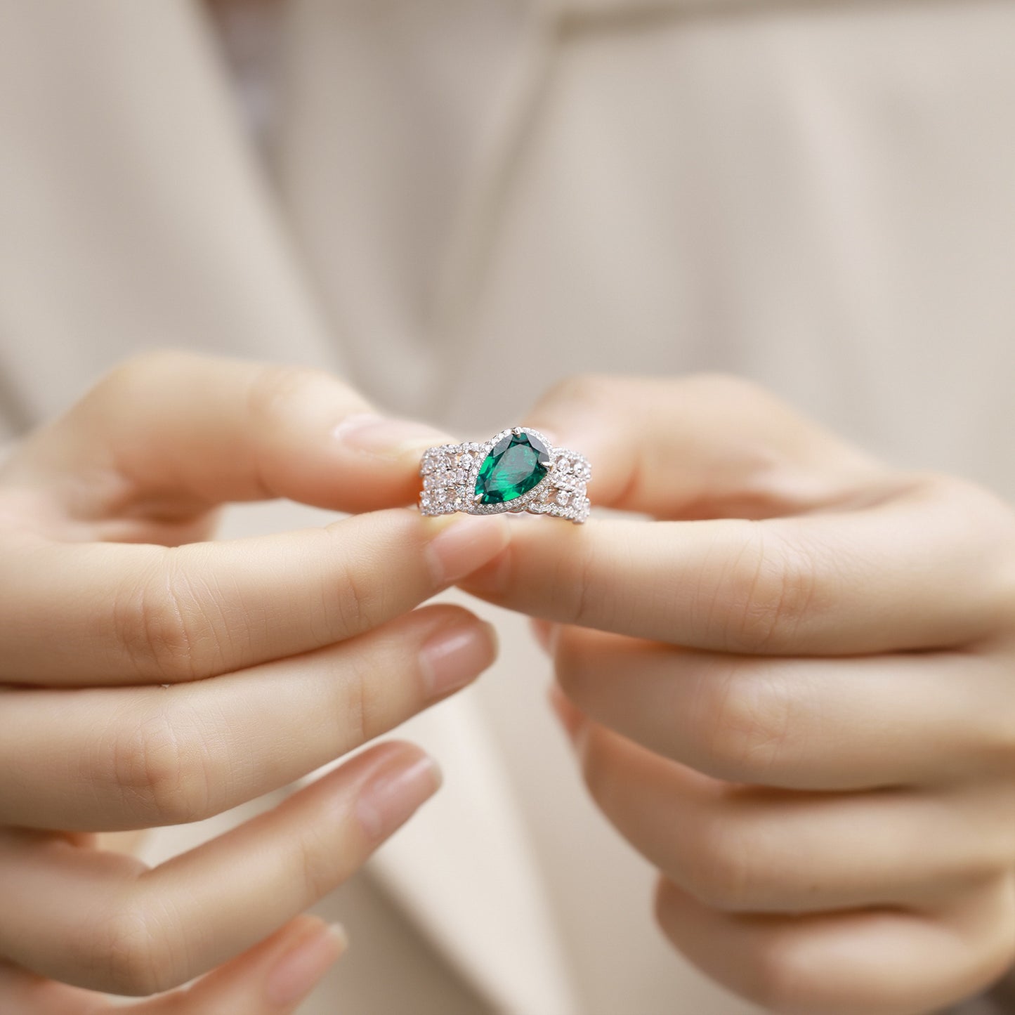 Close-up held in hands, luxury 2-piece pear-cut emerald stackable statement ring under soft lighting.