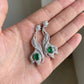 Close-up held in hand, 3.14ct oval-cut emerald wave earrings, intricate halo details.