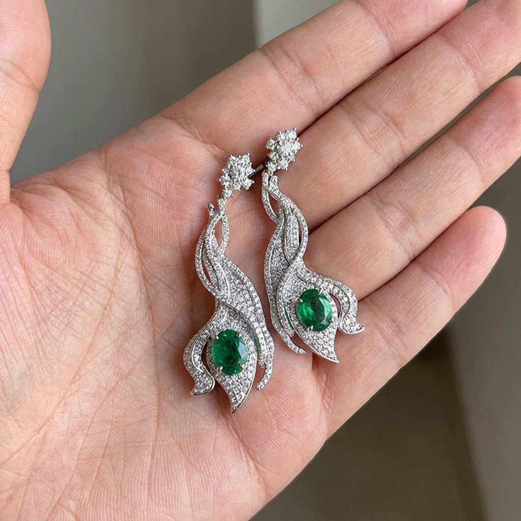 Close-up held in hand, 3.14ct oval-cut emerald wave earrings, intricate halo details.