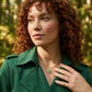 A model demonstrating a layered necklace look with the Kendra Scott green clover gold pendant against a green trench coat
