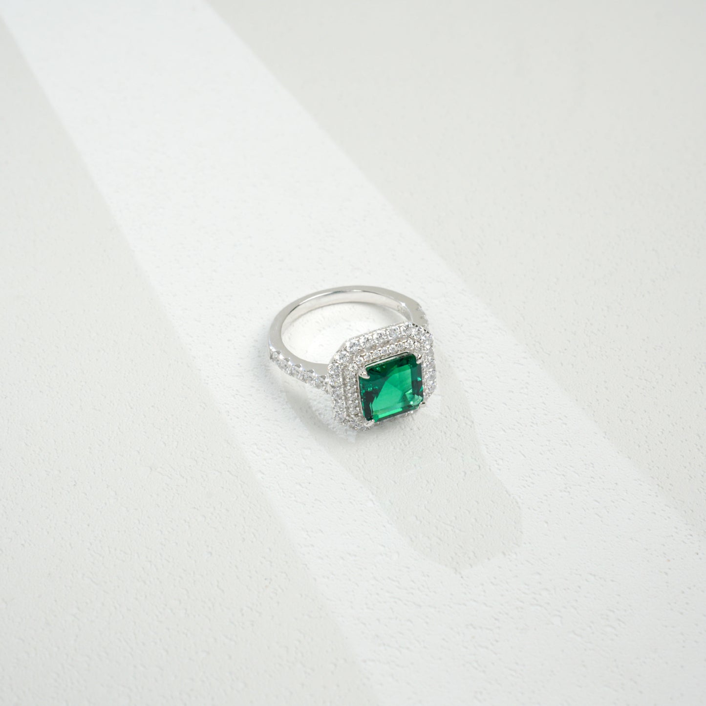 Macro close-up product view of a fine jewelry emerald double halo ring with a diamond encrusted split-shank pave band.