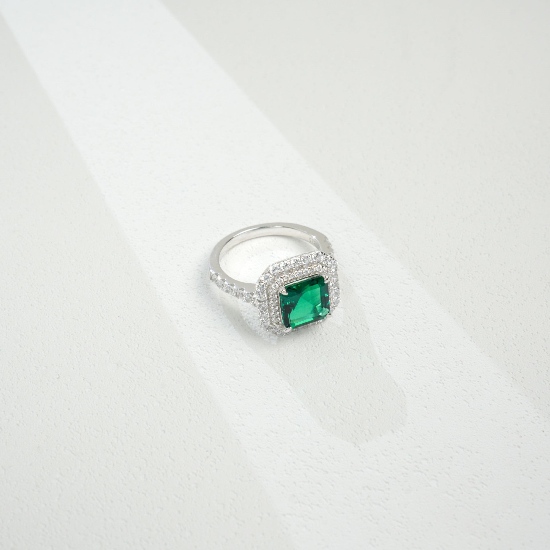 Macro close-up product view of a fine jewelry emerald double halo ring with a diamond encrusted split-shank pave band.