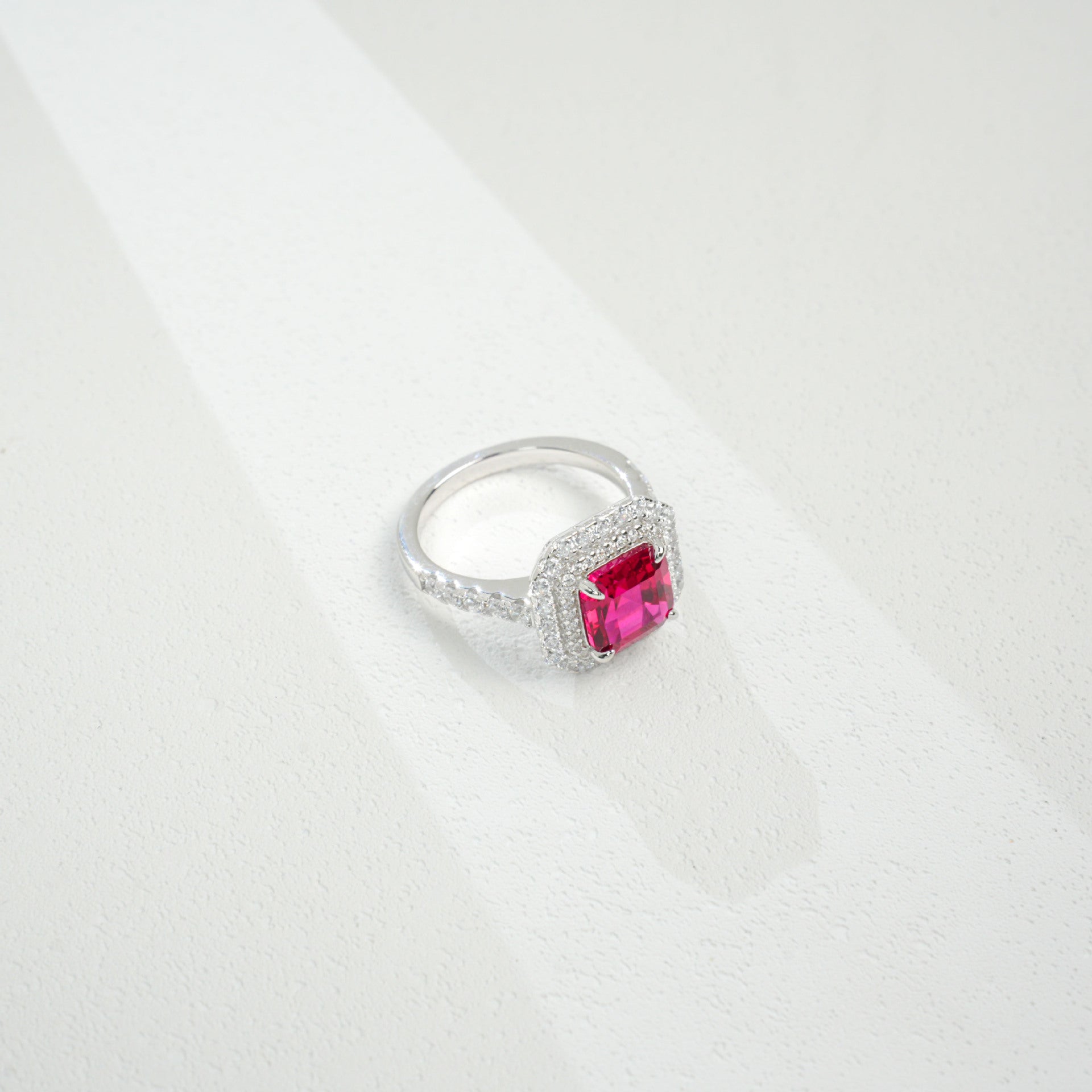 Macro close-up product view of a fine jewelry ruby double halo ring with a diamond encrusted split-shank pave band.