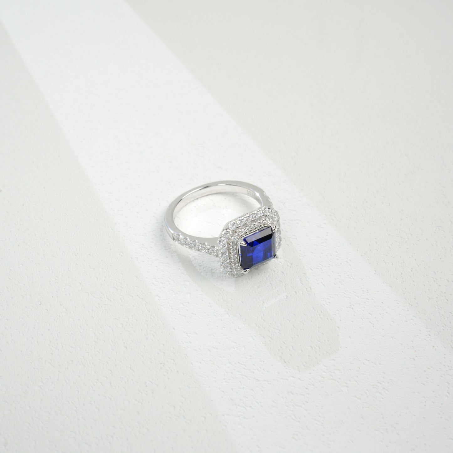 Macro close-up product view of a fine jewelry sapphire double halo ring with a diamond encrusted split-shank pave band.