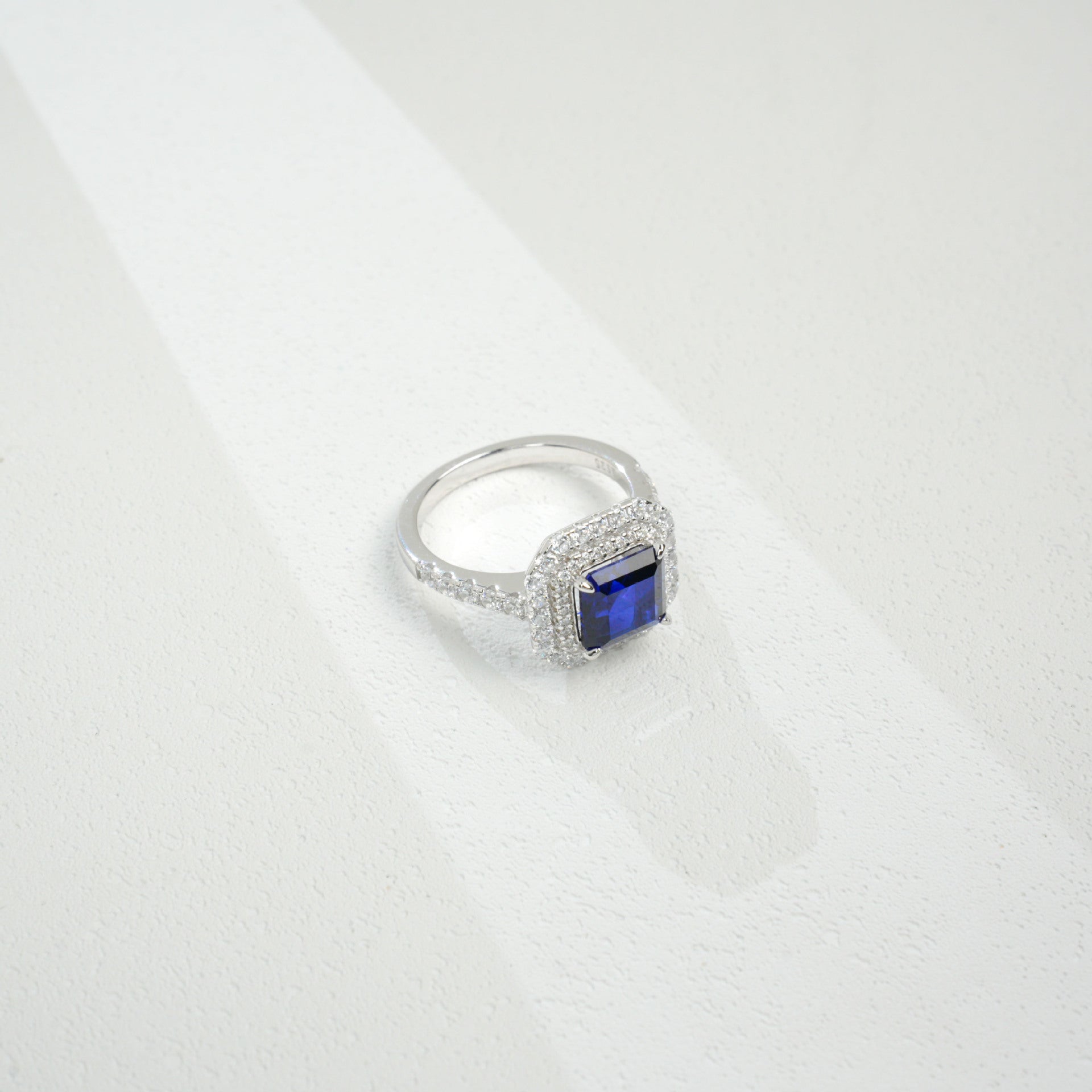 Macro close-up product view of a fine jewelry sapphire double halo ring with a diamond encrusted split-shank pave band.