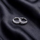 Pair of five stone round brilliant lab grown diamond huggie hoop earrings resting flat on dark black silk