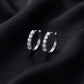 Pair of five stone round cut lab grown diamond huggie hoop earrings standing upright on dark black silk
