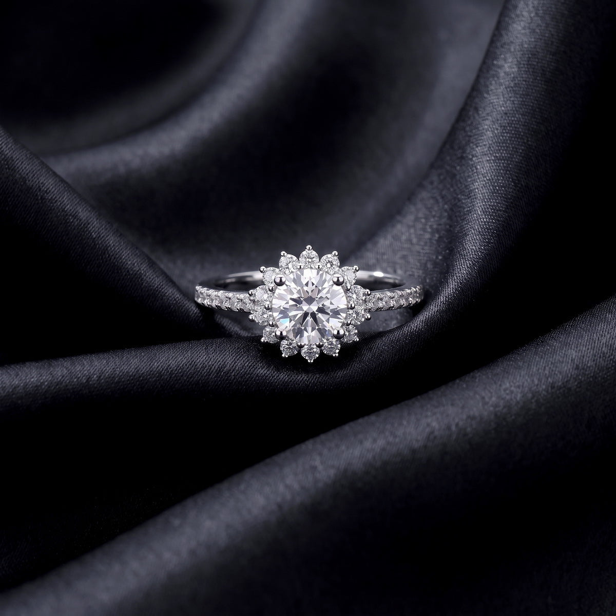 Front view of floral sunburst halo lab grown diamond engagement ring resting on dark black silk