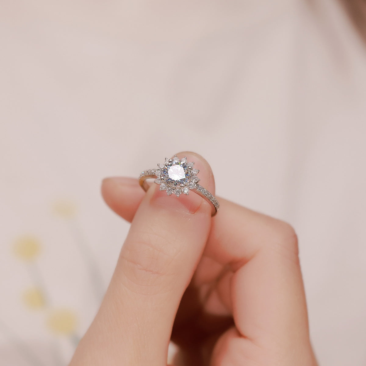 Close up of hand holding floral sunburst halo lab grown diamond ring in warm natural lighting