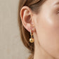 Side close-up view of a model wearing gold ball charm moissanite huggie hoop earrings.