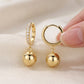 Hand holding gold ball charm moissanite huggie hoops showing snap-hinge closure.