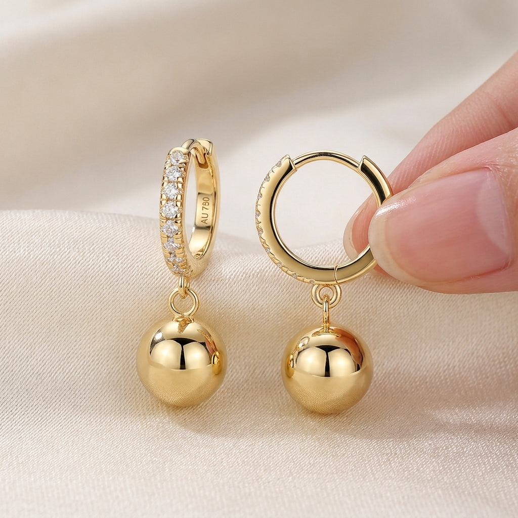 Hand holding gold ball charm moissanite huggie hoops showing snap-hinge closure.