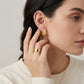 Model wearing gold textured leaf chunky huggie moissanite earrings in a close-up lifestyle shot.