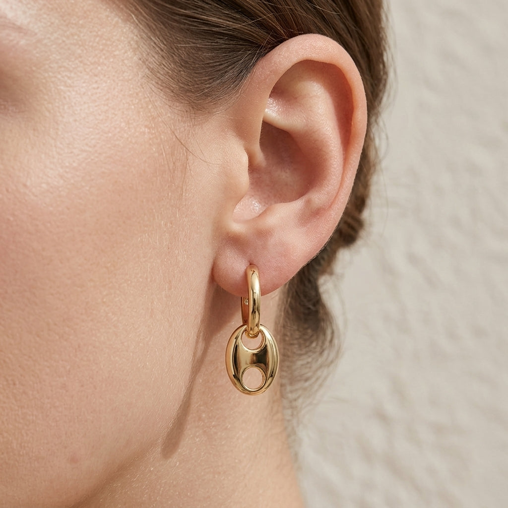 Close-up view of a model wearing classic gold anchor link dangle hoop earrings.