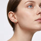Model wearing gold round cut moissanite four-leaf clover cluster halo studs in a daylight portrait.