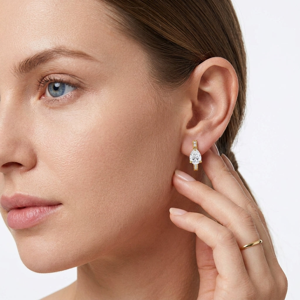 Model wearing gold pear shaped moissanite huggie hoop earrings in a lifestyle portrait.