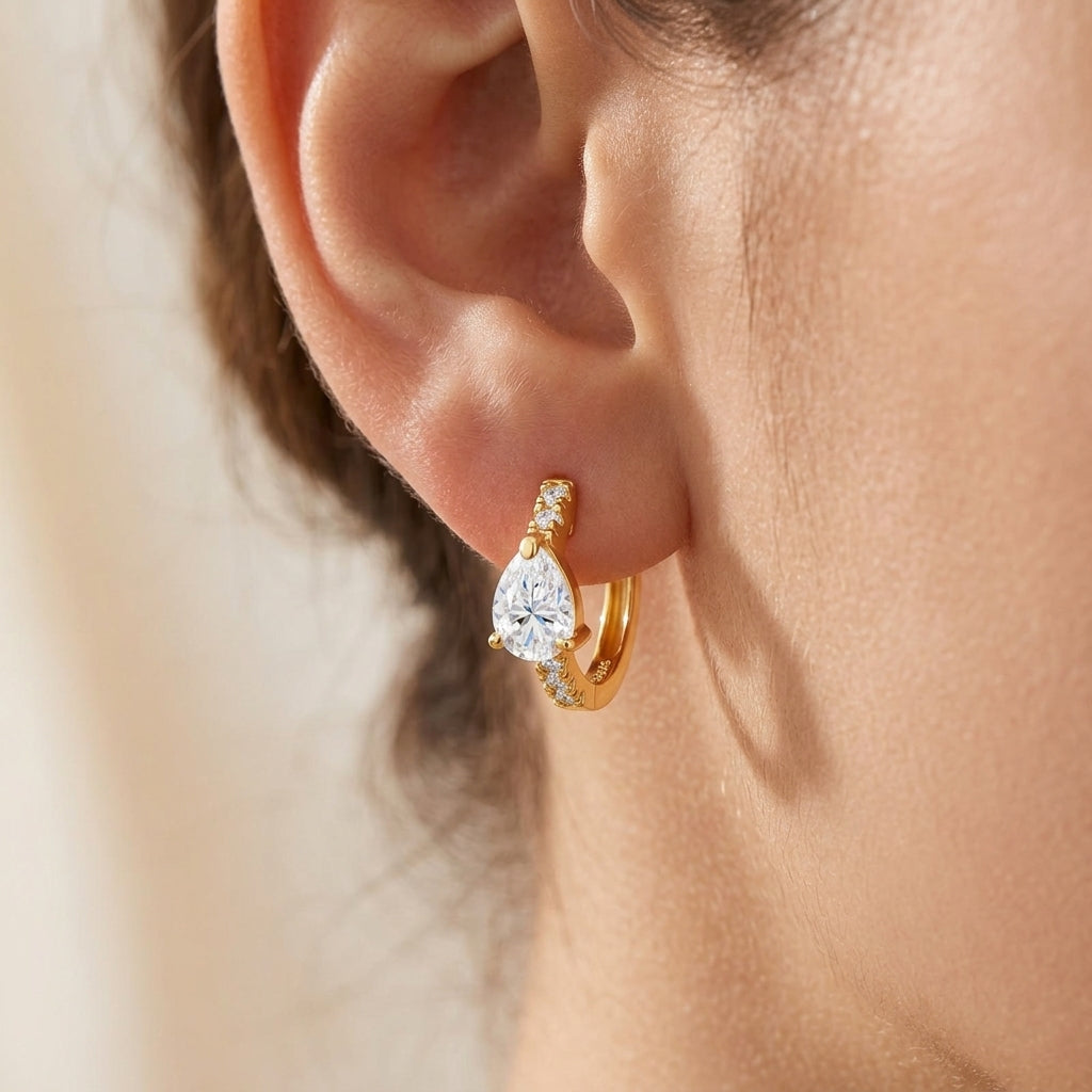 Close-up view of a model wearing gold pear cut moissanite huggie hoop earrings.