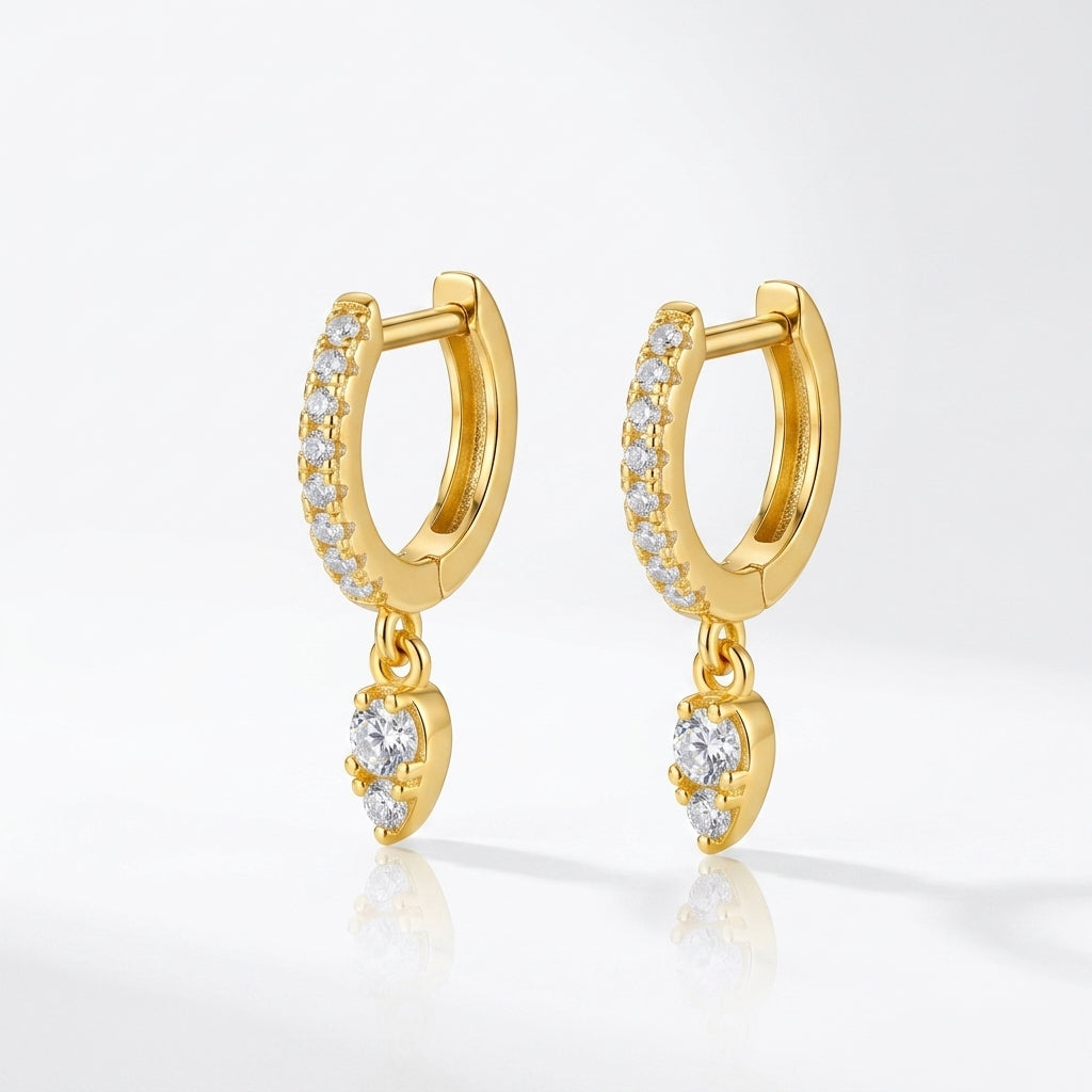 Pair of gold pavé moissanite huggie hoops with pear-shaped teardrop charms.